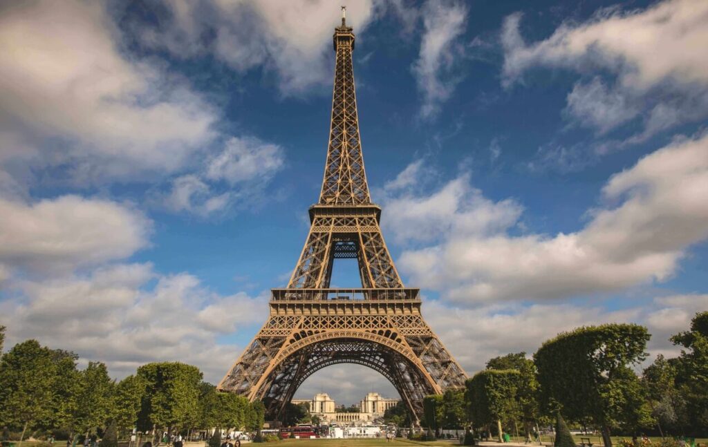Eiffel Tower seen from the Champ de Mars against a blue sky with clouds, Paris